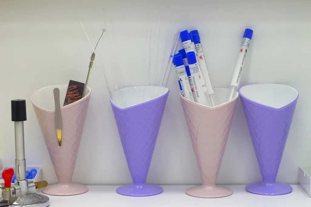 Four pastel cone-shaped lab caddies holding glass capillary rods and plastic-tipped transport swabs.